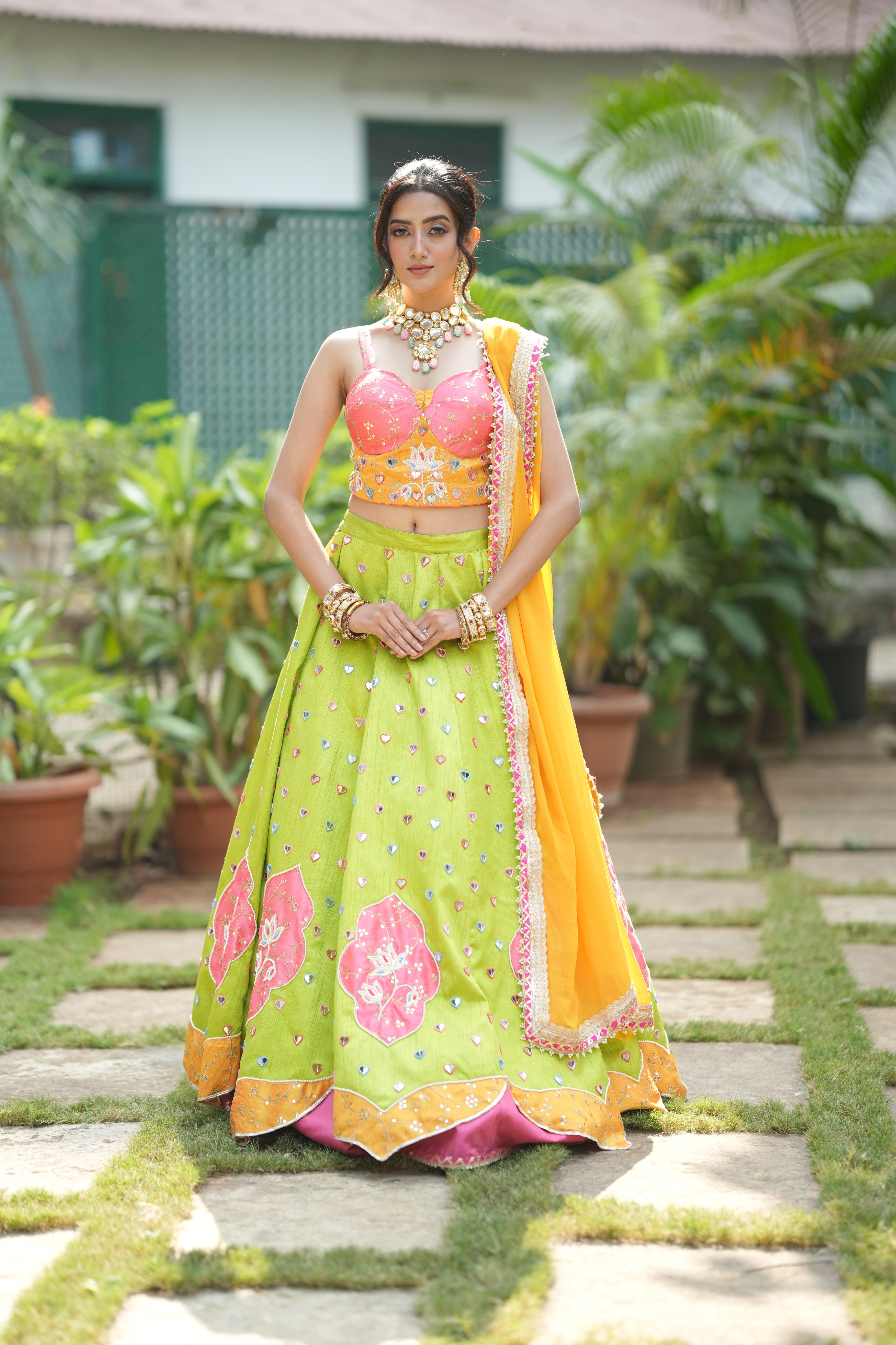 Woman smiling and posing in a festive lehenga with intricate embroidery and ethnic jewelry.