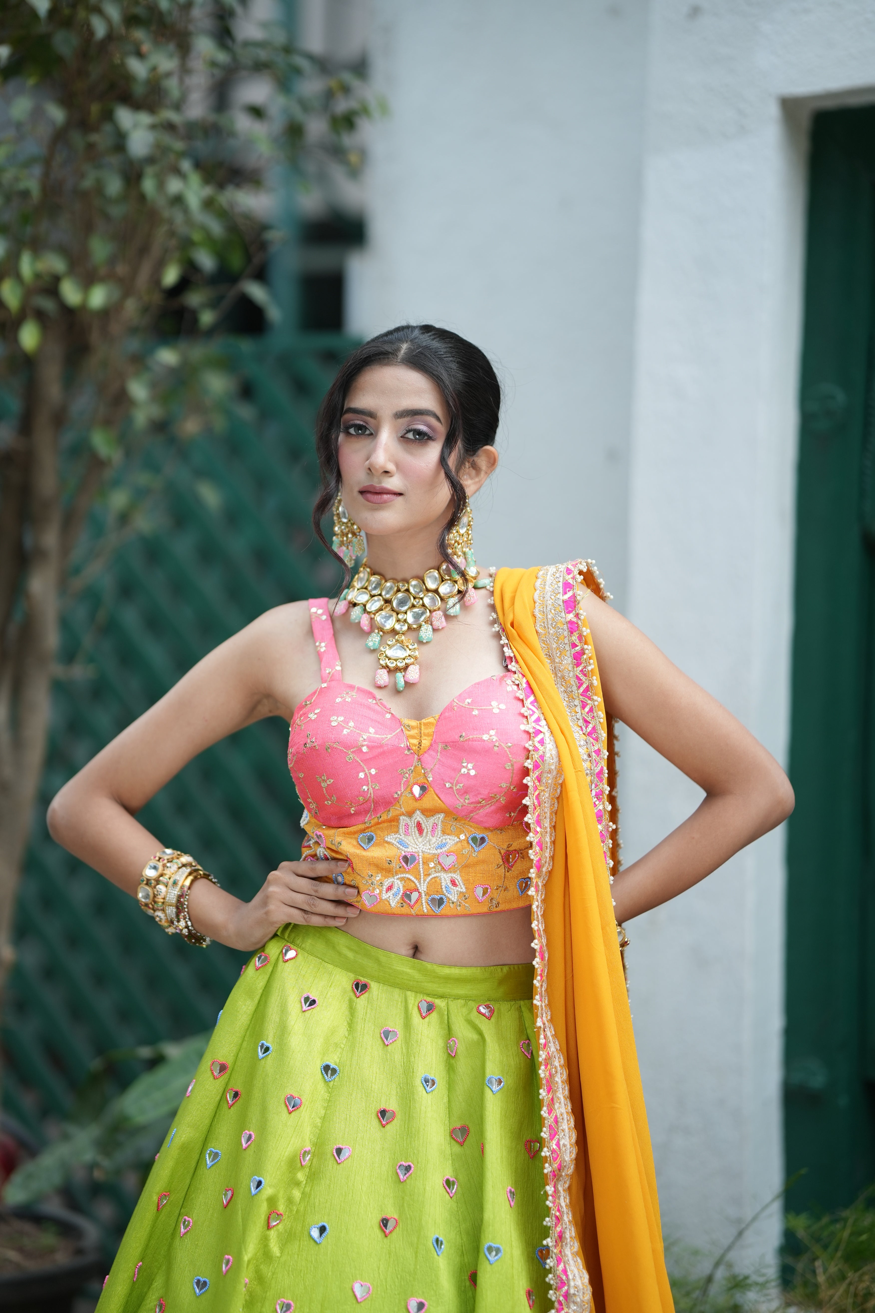 Close-up of a woman in a pink embroidered blouse and orange dupatta with statement jewelry and festive makeup.