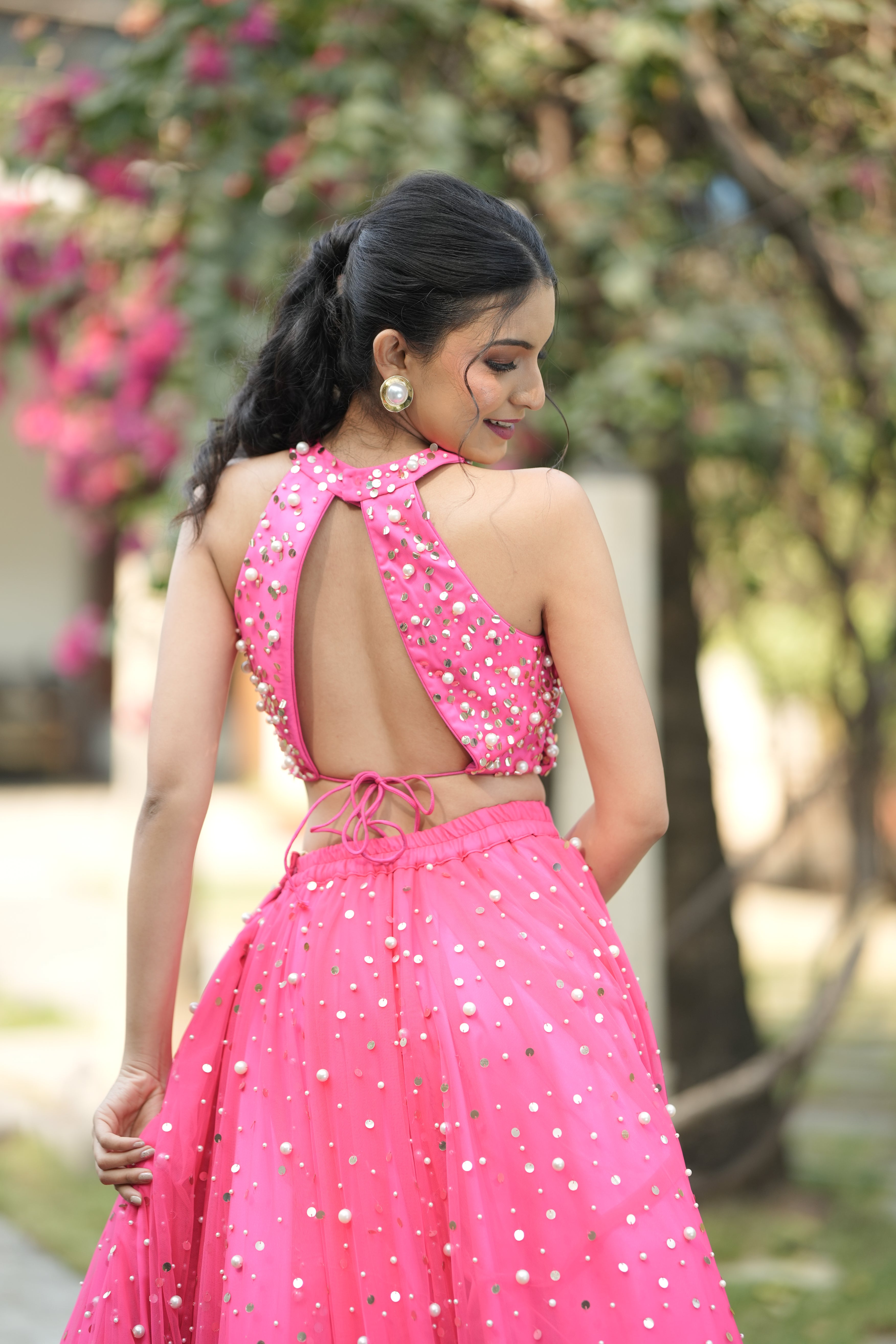 Pink crop top lehenga styled with jewelry and potli bag for wedding party.