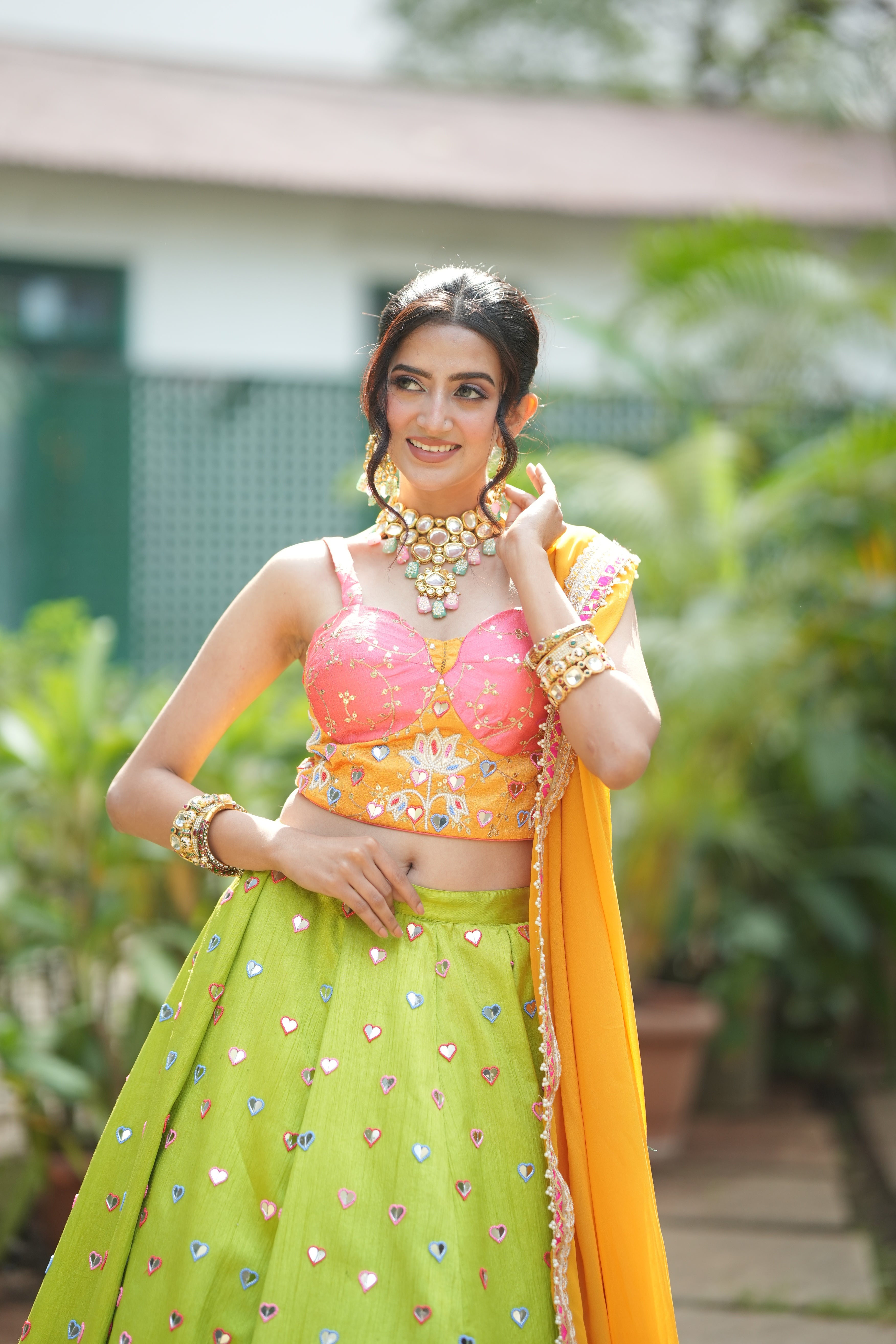 Woman in a brightly lit setting wearing lehenga with lotus motifs, accessorized with bangles and a statement necklace.
